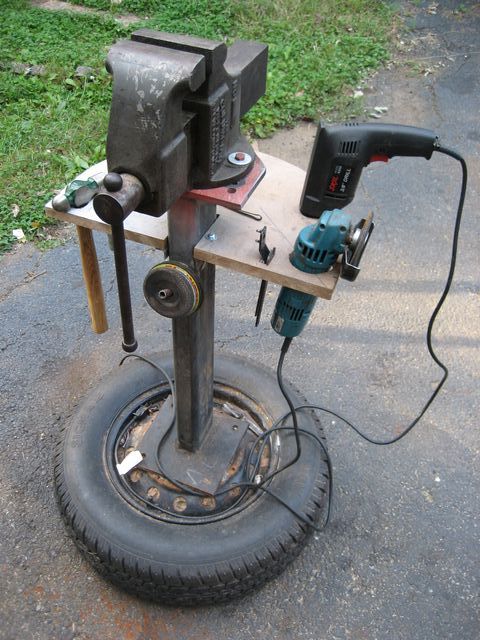 A homemade vise stand crafted from an old tire, featuring a metal vise attached to a wooden base with tools and accessories.