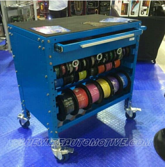 Blue cart with black top and drawer, filled with colored wire spools on wheels.