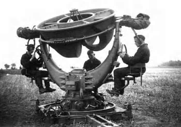 Four men in military attire operating a large, rotating black-and-white radar dish outdoors.