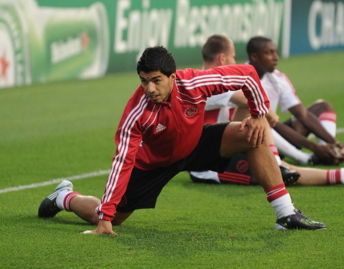 Man in red jacket stretching on field.