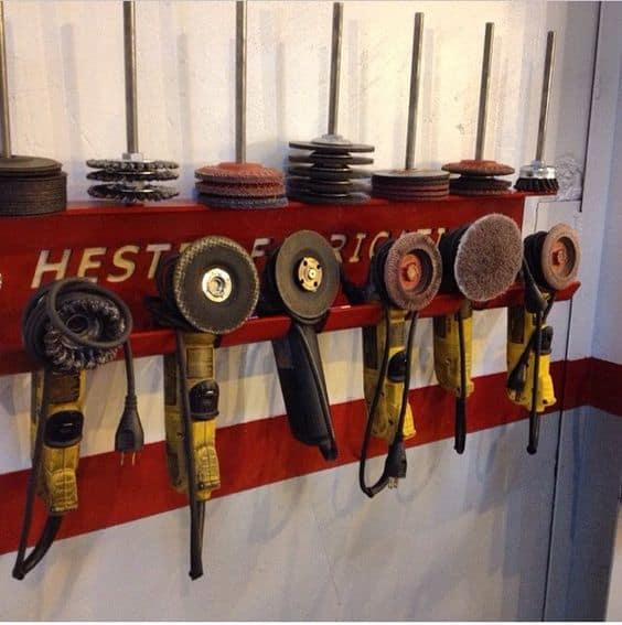 Angle grinders and attachments on a red tool holder against a white wall.