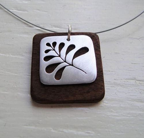 A square wooden pendant with a silver cutout design featuring a leaf motif.