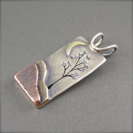 Silver pendant with engraved tree design against night sky backdrop.