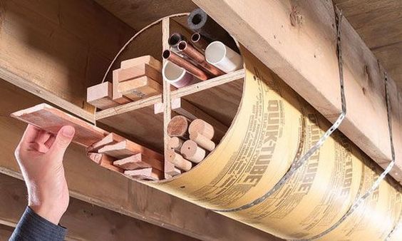 Hand holding wooden shelf with assorted objects above insulated pipe.
