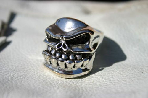 Silver skull ring with intricate details on face, teeth, and jawline.
