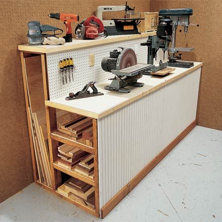 A well-organized workshop with a pegboard wall, various tools, a drill press, bandsaw, and lathe, along with storage solutions like drawers and shelves.