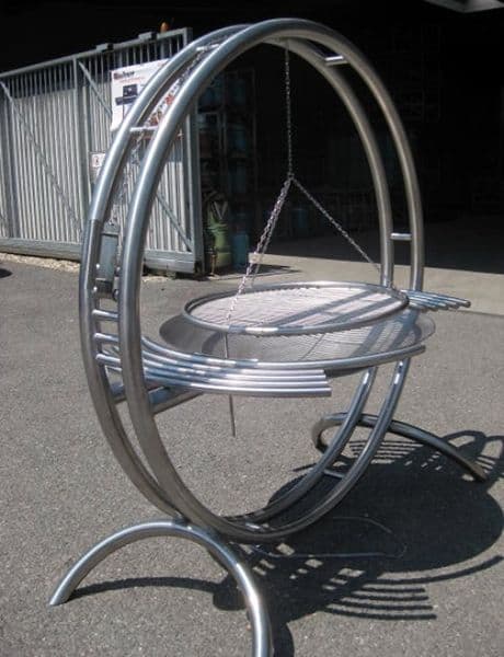 Stainless steel BBQ grill with curved, circular design and suspended chain.