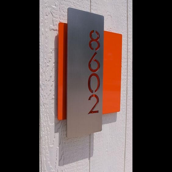 A modern house number sign with silver and orange panels on a white wall.