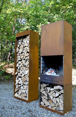 Rustic outdoor fireplace with weathered copper exterior and stacked firewood.
