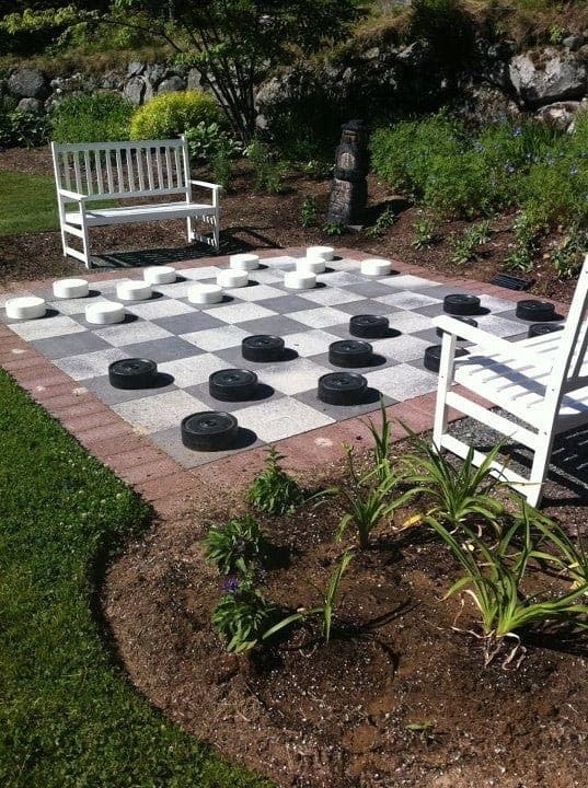 Oversized checkers pieces on an outdoor checkerboard in a garden setting.