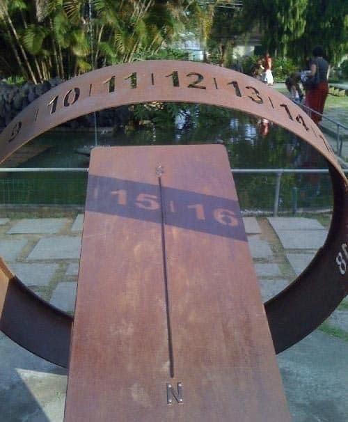 A rusted outdoor sundial with numbered top edge and shadowed lower section.