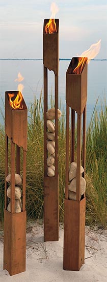 Tall wooden torches on a sandy beach with flames and swaying grasses in the background.