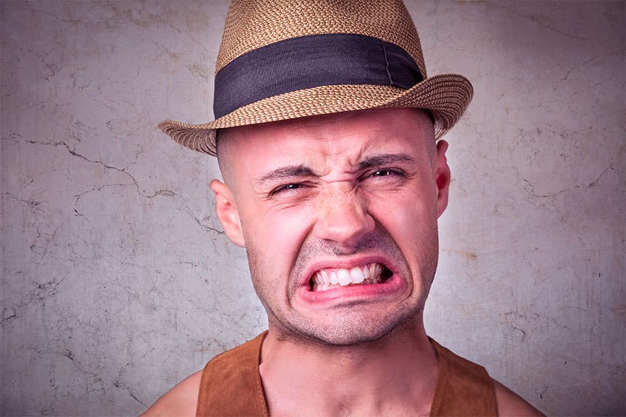 Man with frustrated expression, wearing tank top against gray wall.