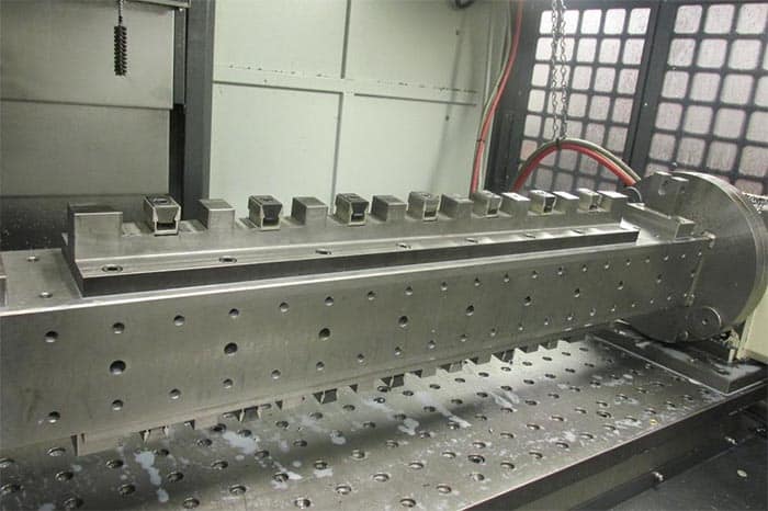 Large metal fixture on machine table with base plate, clamping blocks and holes, factory setting.