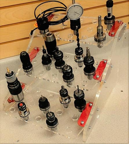 Transparent plastic benchtop rack with various tools and parts attached.