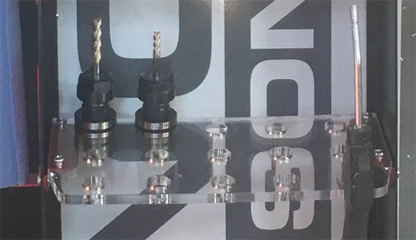 Close-up photograph of two drill bits on a clear acrylic shelf with UNISON branding.