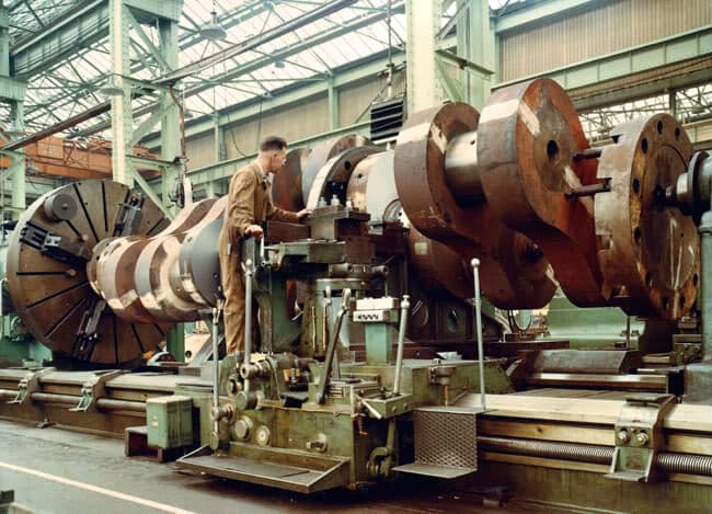 Industrial lathe in factory setting with operator and multiple spindles.