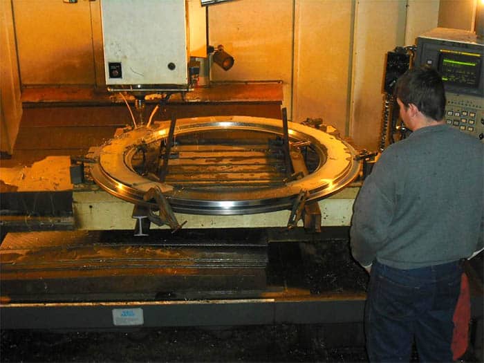 A large metal ring on a CNC lathe or milling machine in a cluttered workshop.
