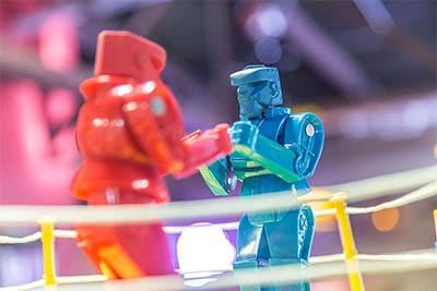 Two small plastic robots facing each other behind ropes, one red and one blue.