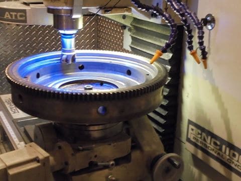 Large metal gear being machined with CNC machine, spindle rotating on two axes.