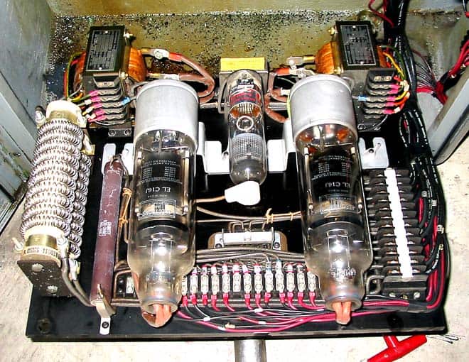 Industrial electrical device interior with complex wiring, tubes, and metal components on a concrete floor.