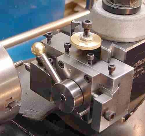 A close-up of a metalworking lathe's threading tool holder with a brass ball on the end of an attached rod.