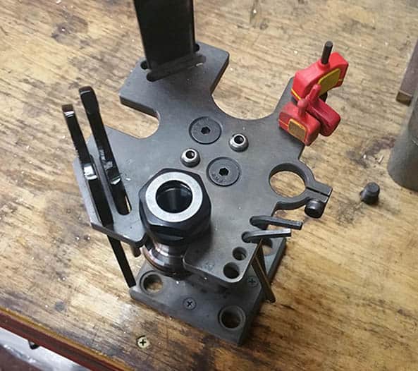 Black metal fixture on wooden table, with central hole, smaller holes, and a red handle.