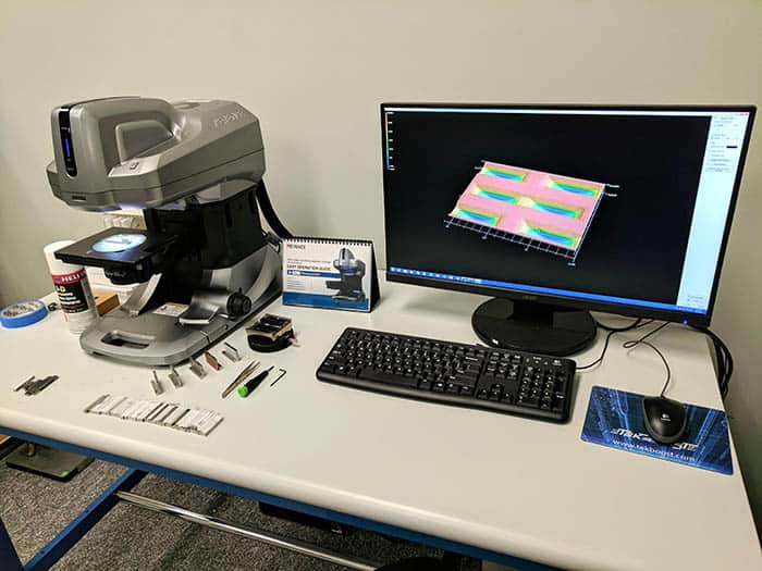 A photograph of precision measurement and inspection tools, including a microscope, computer equipment, and other instruments.