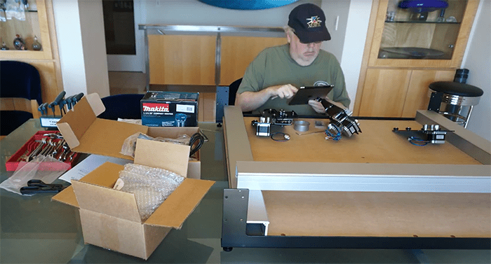 Man in green shirt working at a desk with various tools and equipment.
