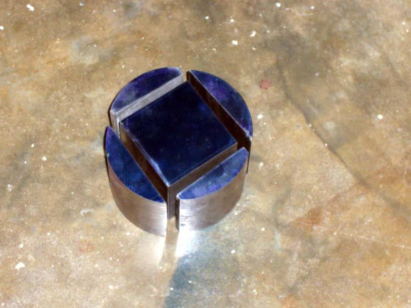 Small, round metal object with 4 curved sections cut out.