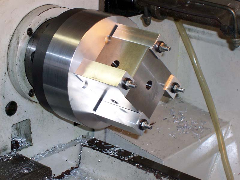 Silver metal part with circular base and rectangular top secured by four bolts.