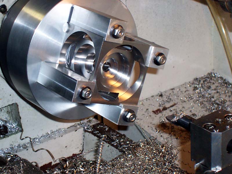 Metal part being machined on CNC lathe with visible metal shavings.