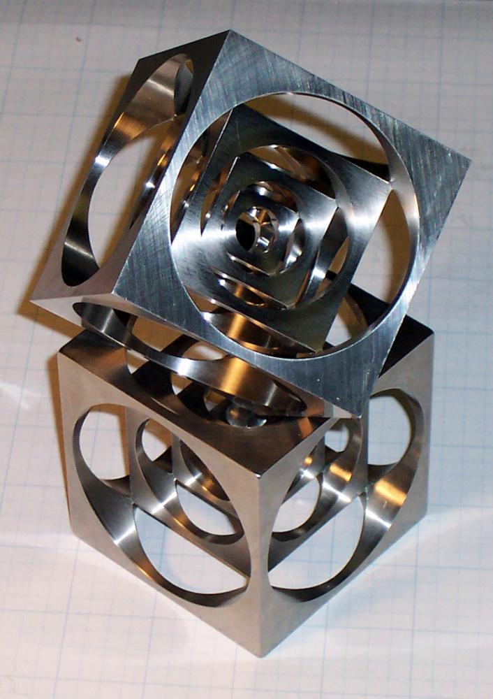 Stainless steel or aluminum geometric sculpture with interconnected cubes and circular cutouts in a staggered arrangement.