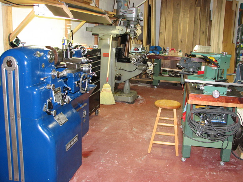 Cluttered workshop with various machines, including a Monarch metal lathe and drill press.