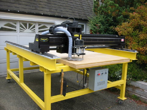 Large black router table with yellow frame and gray top on a driveway.