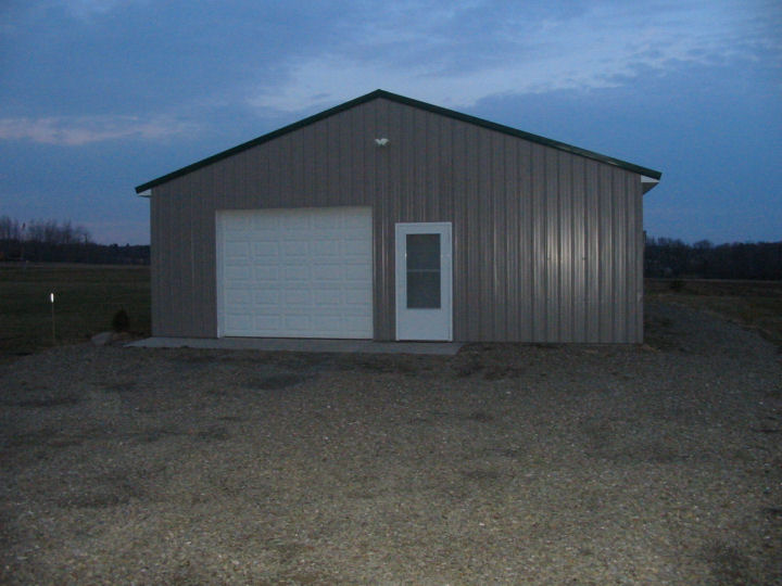Gray metal building with white garage door and smaller windowed door set against blue sky with clouds.