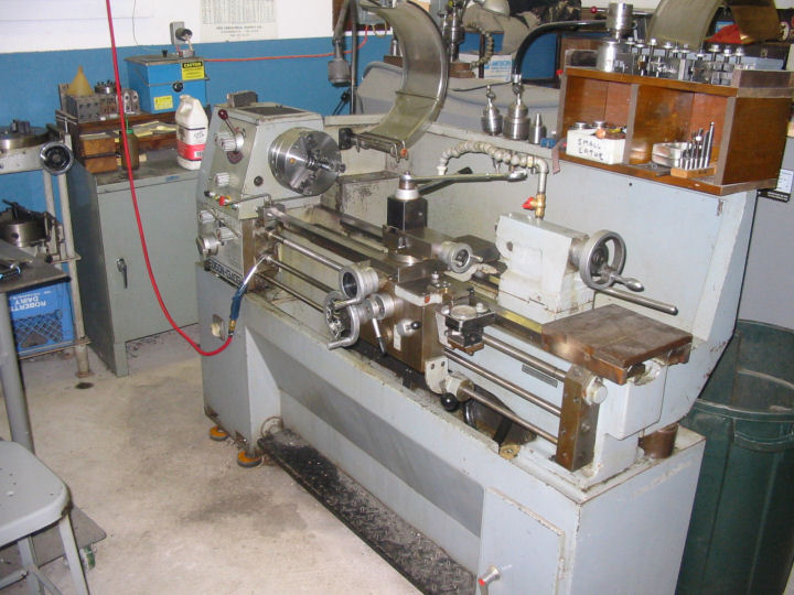 Gray metal lathe on concrete floor with tools and components.