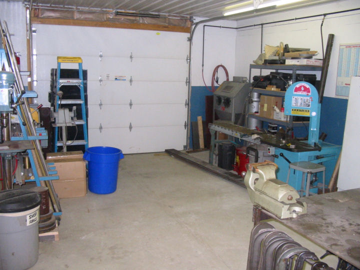 Well-lit workshop with tools and equipment, including metal table, tool cabinet, shelving unit, press machine, lathe, and milling machine.