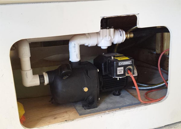 Black Everbilt submersible pump with red cord, installed in white box on light wood floor.