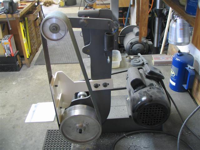 Shop bench-top belt sander with black metal frame and adjustable arm.
