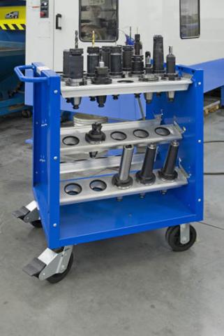 Blue tool cart with various tools and equipment on its surface, positioned in front of a white wall in an industrial workshop setting.