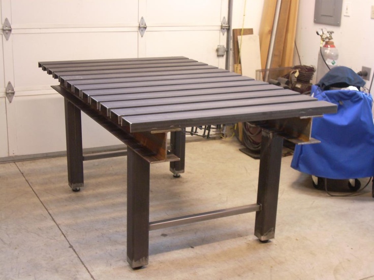 A sturdy steel clamping table with a slatted top and rolling base in a workshop setting.