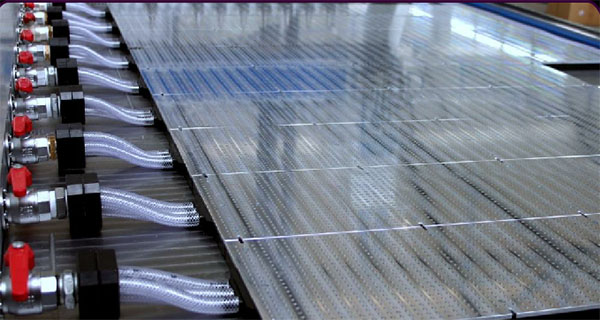 Metal surface with rows of small holes and industrial pipes.