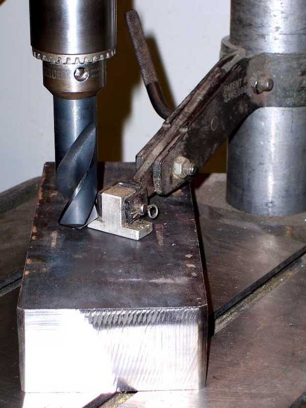A drill press vise clamp secured by a spring-loaded mechanism on an aluminum block with a metal base.