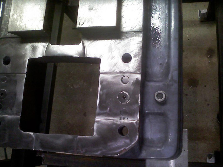 A metal part with various holes and cutouts, possibly made of steel or aluminum.
