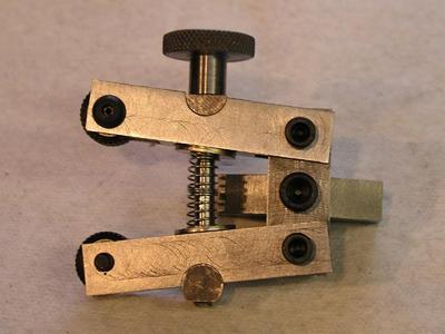 Metallic knurling device with black knob and spring-loaded mechanism.