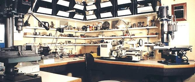 Well-organized metalworking workshop with milling machine, lathe, and other equipment on shelves against a white wall background.