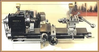 Old-fashioned lathe with large cylindrical drum on plain background.