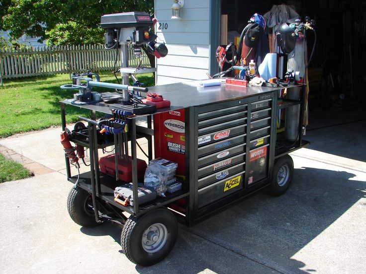 A mobile workshop featuring a large toolbox with multiple drawers and shelves, equipped with various tools and a drill press.