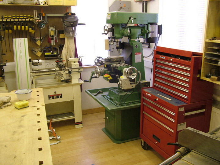 Well-organized workshop with drill press, table saw, and tool chest on a light-colored wood floor.